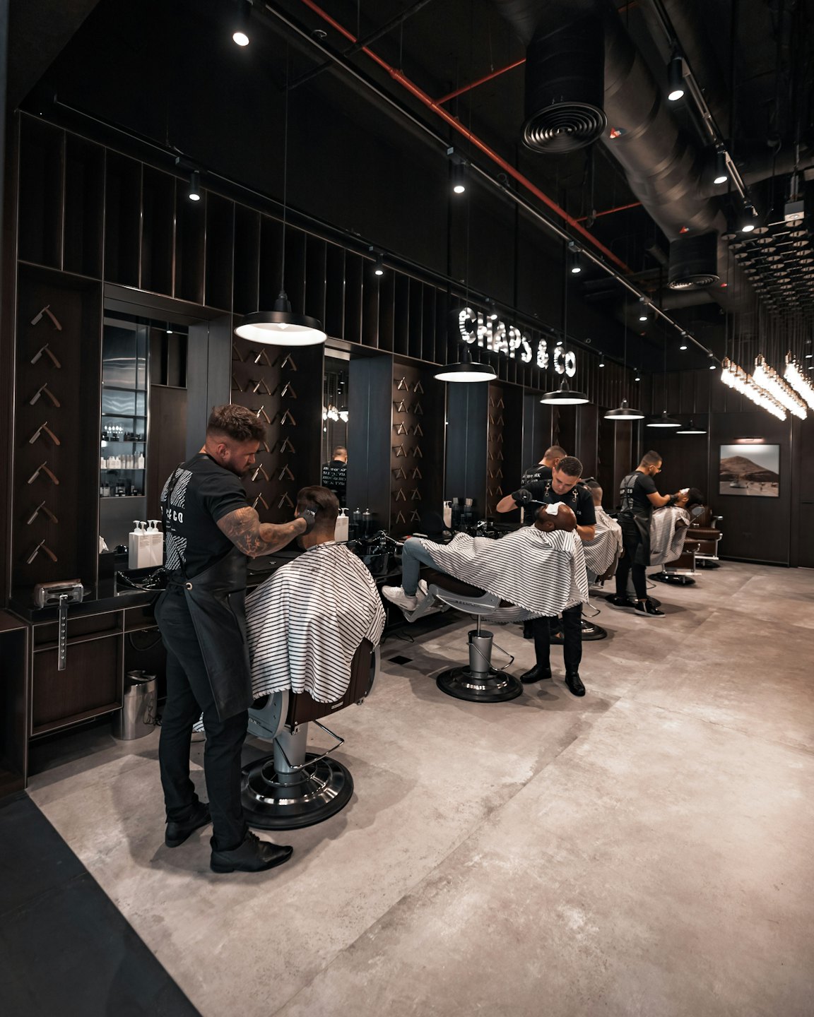 Barberos cortando el pelo en una barbería moderna y concurrida.
