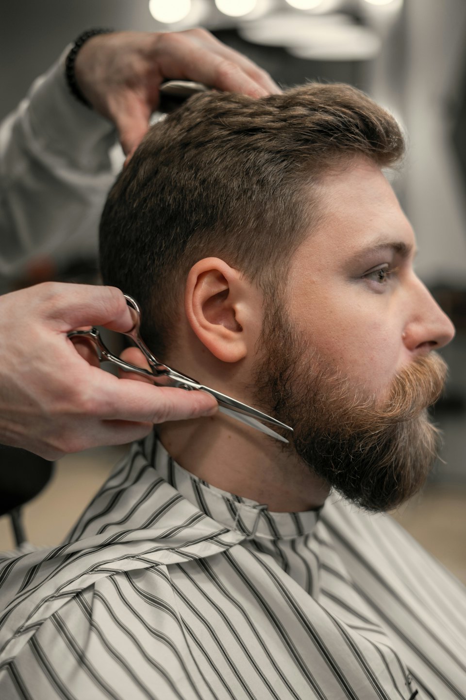 Barbero recorta barba pelirroja a un hombre con capa a rayas.